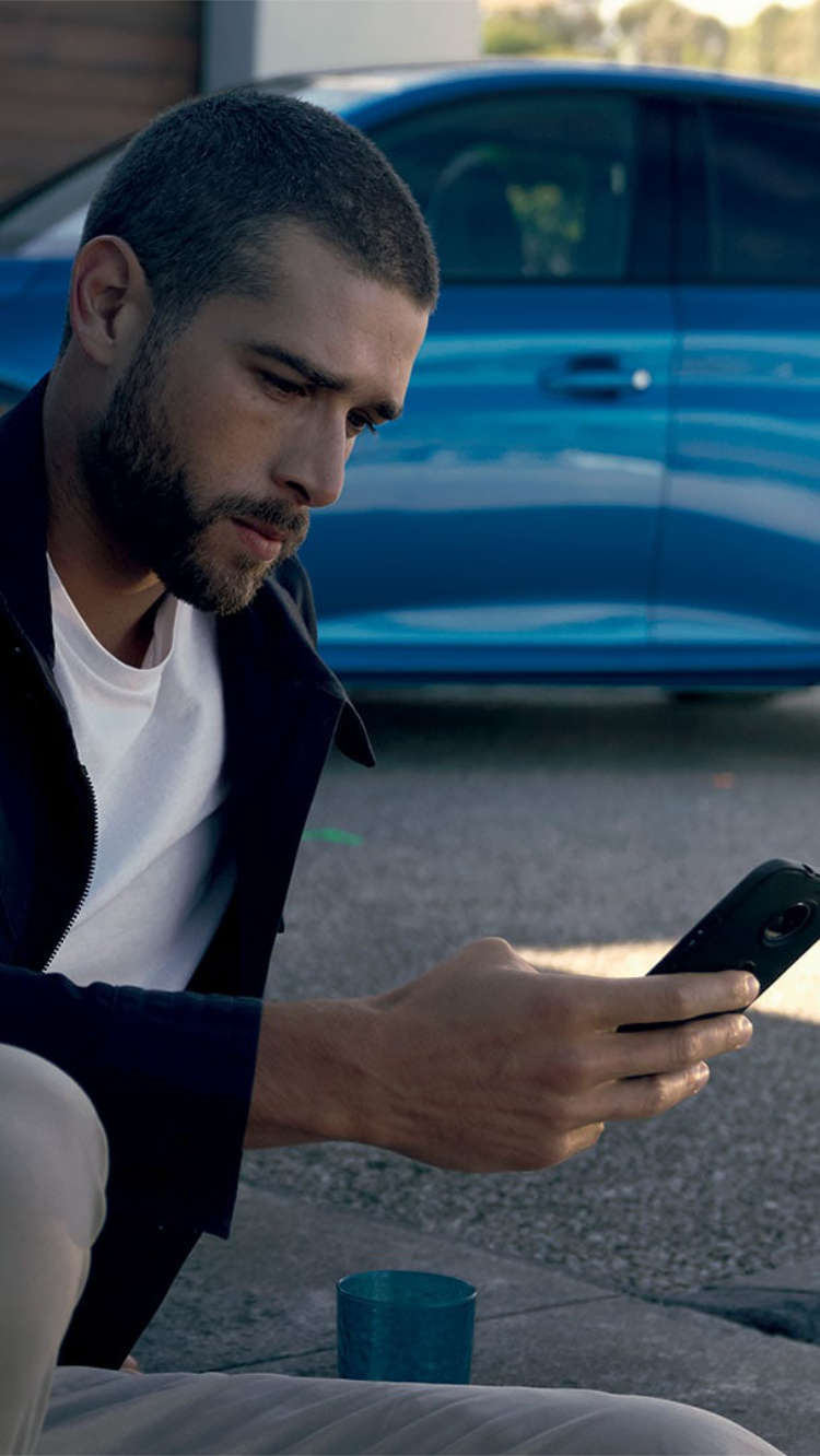 Чоловік дивиться на екран смартфона біля автомобіля Peugeot